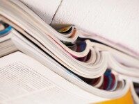 Gestapelte, aufgeschlagene Magazine auf weißem Holztisch, Symbol für Printmedien oder Verlagswesen.