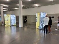 Personen gehen durch eine Ausstellung mit beleuchteten LED-Säulen anlässlich des Unijubiläums
