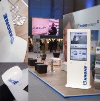 Multimedialer Messestand mit eleganten Designdisplays für Krone. Moderner Messestand mit weißen Designdisplays und digitaler Präsentationsstele der Firma Krone, umgeben von Sitzmöbeln und Messebesuchern.
