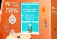 Interaktive Station „Wasser Ziehen“ mit Dynascan-Bildschirm. Nahaufnahme der orangefarbenen Spendenstation der Neven Subotic Stiftung mit Infoscreen.