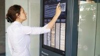 Interaktive Informationsstele mit Touchscreen. Frau bedient interaktive digitale Stele mit großem Touchdisplay, um Informationen aus einer digitalen Bibliothek abzurufen.