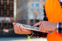 Wrocklage App auf dem Tablet zur Materialverfolgung. Person mit orangefarbener Warnweste bedient Tablet auf Baustelle zur Materialverfolgung.