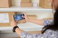 Smartphone-App zur Bestandsaufnahme und Dokumentation. Smartphone-App zur Bestandsaufnahme und Dokumentation im Malerbetrieb, Frau fotografiert Kartons im Lager.