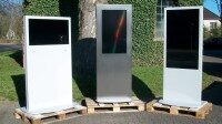 Drei freistehende digitale Werbedisplays auf Holzpaletten im Freien.