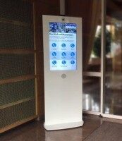 Interaktive Stele im Eingangsbereich eines Gebäudes mit digitalem Bildschirm und Willkommenstext.