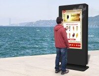 Ein Mann steht vor einem freistehenden Multi-Touch-Bildschirm am Wasser und wählt ein Eis auf dem Bildschirm aus.