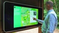 Mann bedient einen großen, wandmontierten Touchscreen mit einer Karte im Freien.