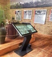 Schwarzer Touchscreen-Kiosk mit geneigtem Bildschirm in einem Museum, zeigt digitale Informationen und Bilder zu Ausstellungsstücken