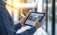Frau mit Maske bedient Smartphone auf Veranstaltung mit unscharfen Messebesuchern und bunten Lichtern im Hintergrund
