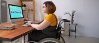 Frau im Rollstuhl arbeitet am Computer mit barrierefreiem Onlineshop auf dem Bildschirm.