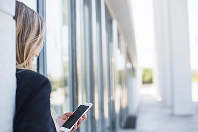 Frau lehnt an Hauswand mit Handy in der Hand Frau lehnt an Hauswand mit Handy in der Hand