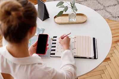 Frau mit Handy schreibt in Planer Frau mit Handy schreibt in Planer