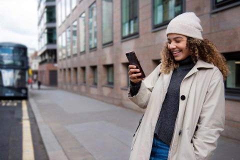 Junge Frau mit Smartphone in der Stadt Junge Frau mit Smartphone lächelt in einer städtischen Umgebung.