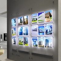 Flyshine Schaufensterwerbung mit mehreren Immobilien-Exposés an einer Wand, Beispiel für hochwertige Innenbeschilderung und Präsentationssysteme