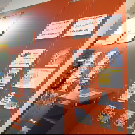 Rote Wand mit transparenten Prospekthaltern und Informationsflyern, Beispiel für funktionale Innenbeschilderung in einer Bankfiliale
