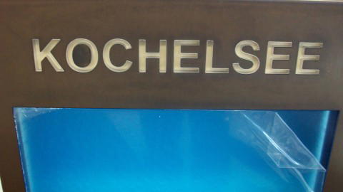 Logo mit dem Schriftzug Kochelsee auf einem bronzenen Schild