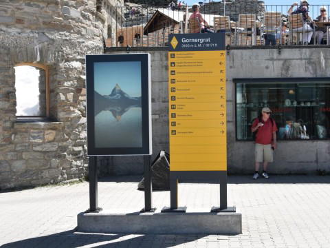 Outdoor Digital Signage Stele am Gornergrat mit Infoscreen Outdoor-Digital Signage Stele mit Display am Gornergrat neben Wegweiser, Hintergrund Matterhorn-Gebiet