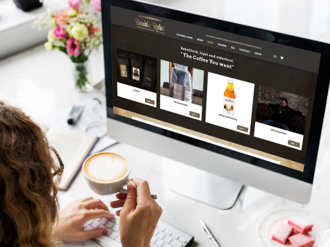 Barista Rebel Online-Shop Ansicht Frau trinkt Kaffee und betrachtet die Website Barista Rebel mit Produktangeboten am Computer