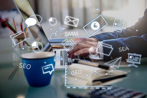 Online-Marketing mit Laptop und Piktogrammen Ein Mann arbeitet an einem Laptop mit Grafiken und Piktogrammen für SEO, SMM, SEA und GEO.