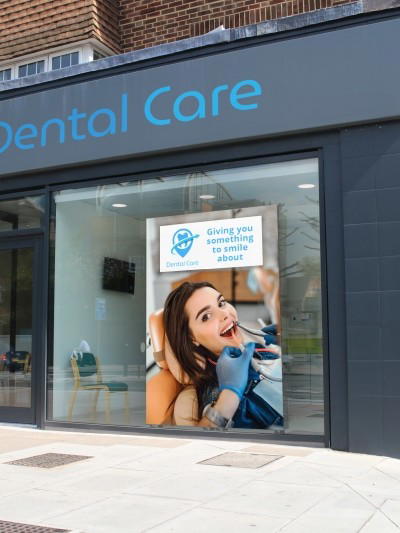 Digital Signage Schaufensterdisplay in Zahnarztpraxis zeigt Werbung mit Patientin und Slogan „Giving you something to smile about“